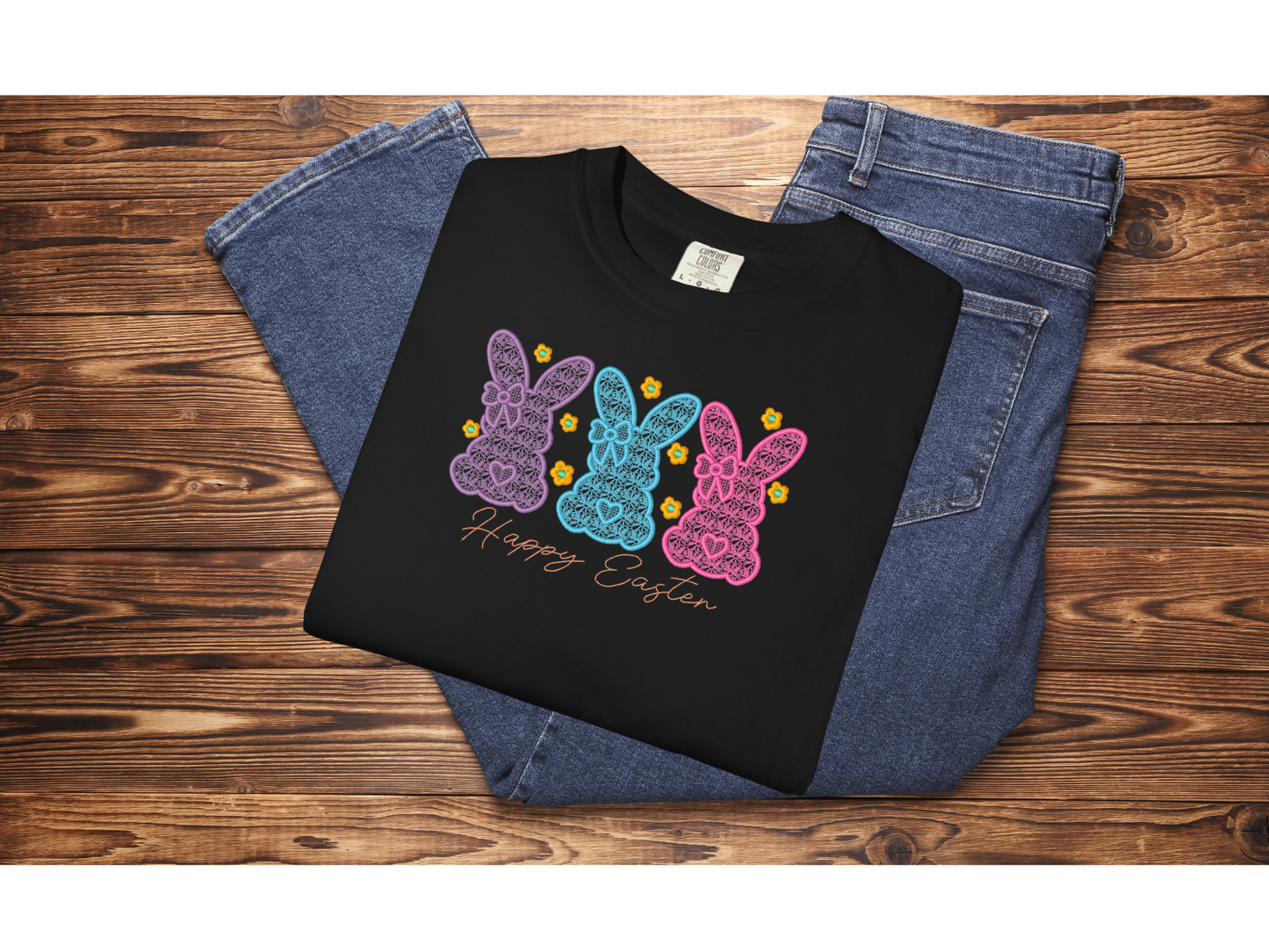 Black sweatshirt with colorful bunny design and 'Happy Easter' text on a wooden surface with jeans.