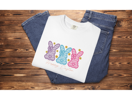 White sweatshirt with colorful bunny design and 'Happy Easter' text on a wooden surface with jeans.
