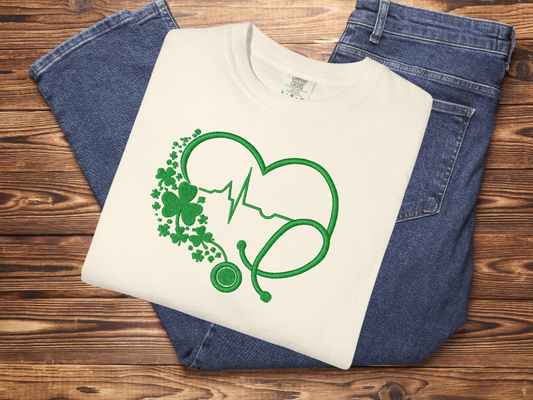 White t-shirt with green graphic design on blue jeans against a wooden background