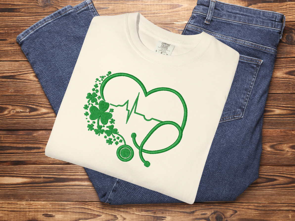 White t-shirt with green graphic design on blue jeans against a wooden background