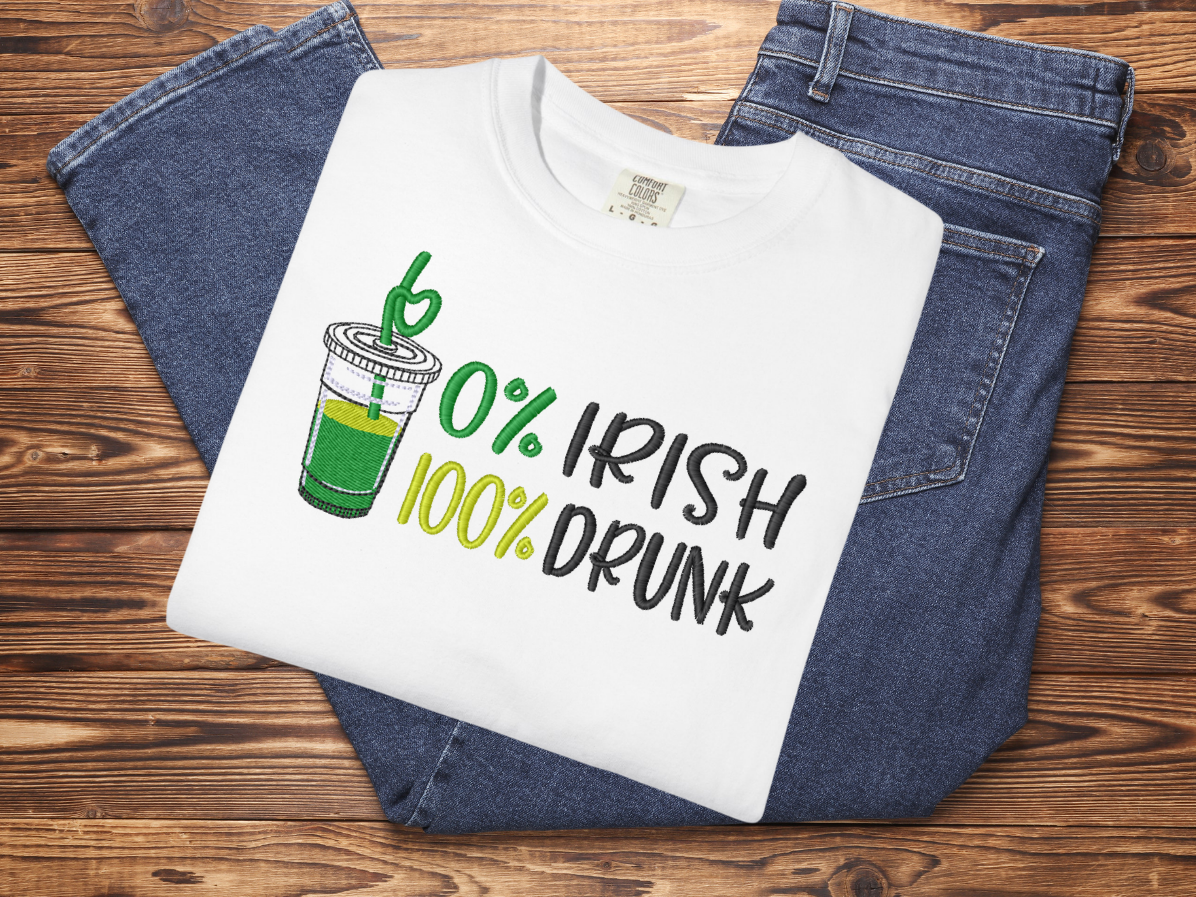 White t-shirt with '0% Irish, 100% Drunk' design on a wooden surface with jeans.