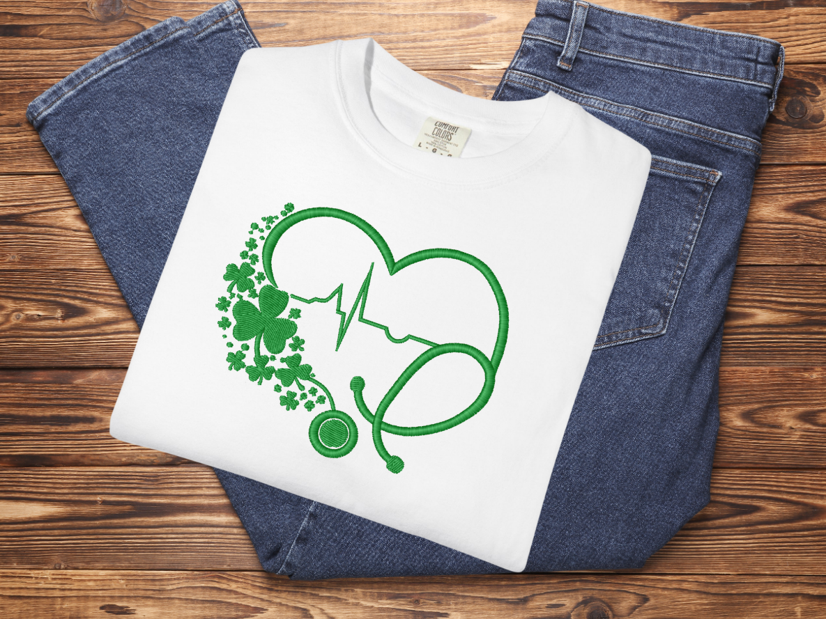 White t-shirt with green medical-themed design on a wooden surface with blue jeans.